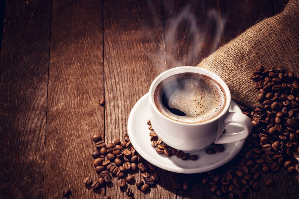 Cup of steaming hot coffee on a wooden surface next to coffee beans