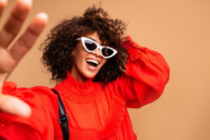 Woman wearing sunglasses smiling on tanish background